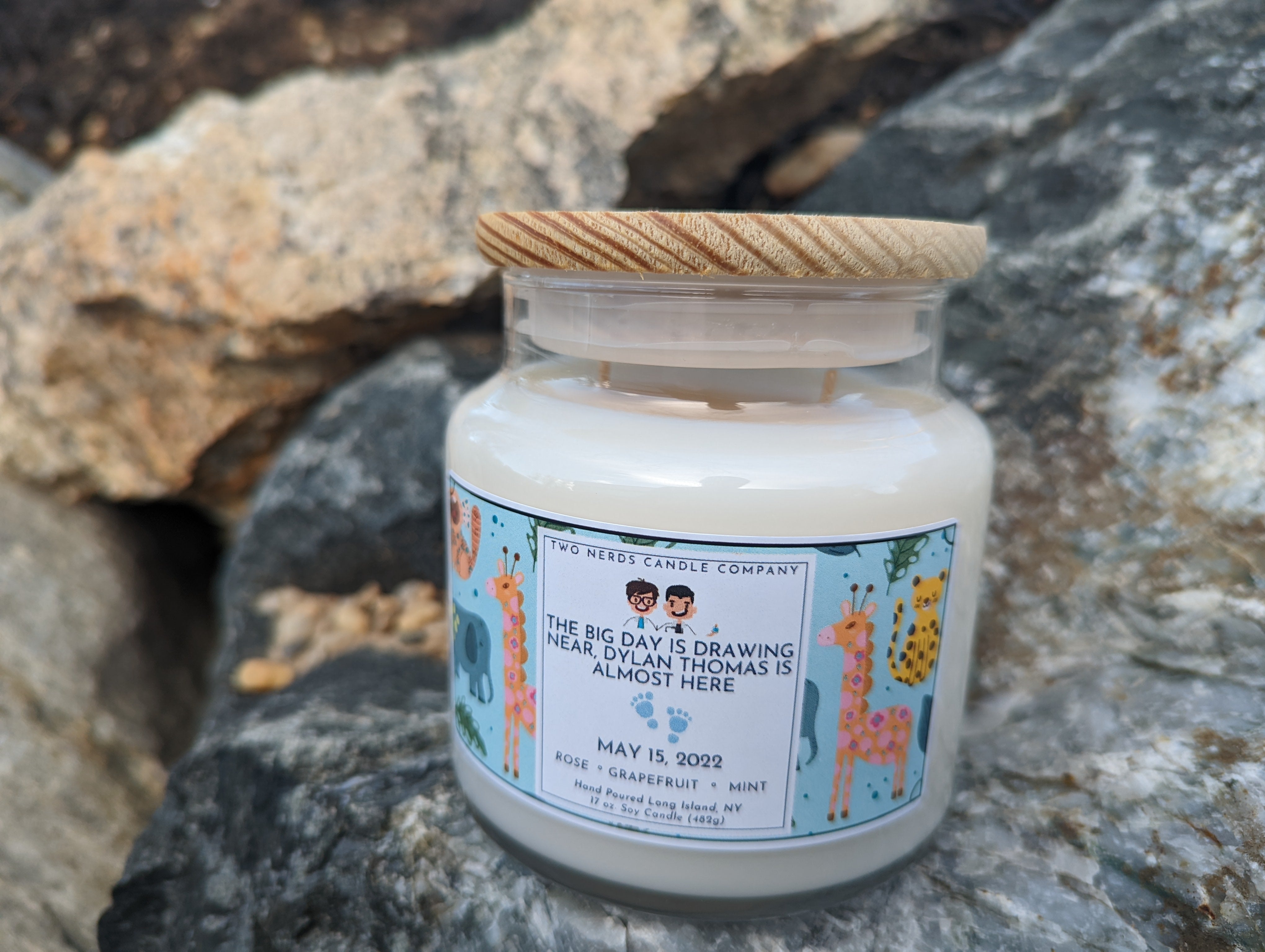 A custom soy candle created for a baby shower. This includes a baby themed background and has the date of the shower with two blue baby feet on the label.