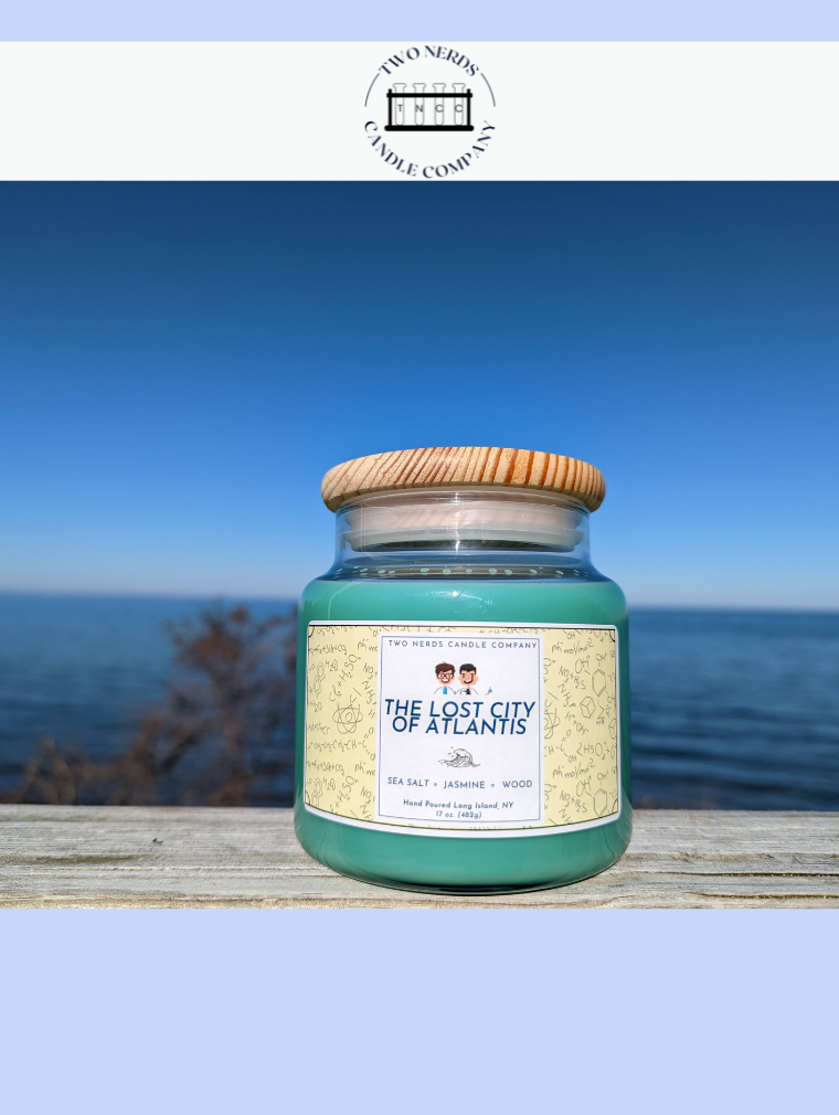 Handmade lost city of atlantis candle in a beach setting with water in the background on a wood table